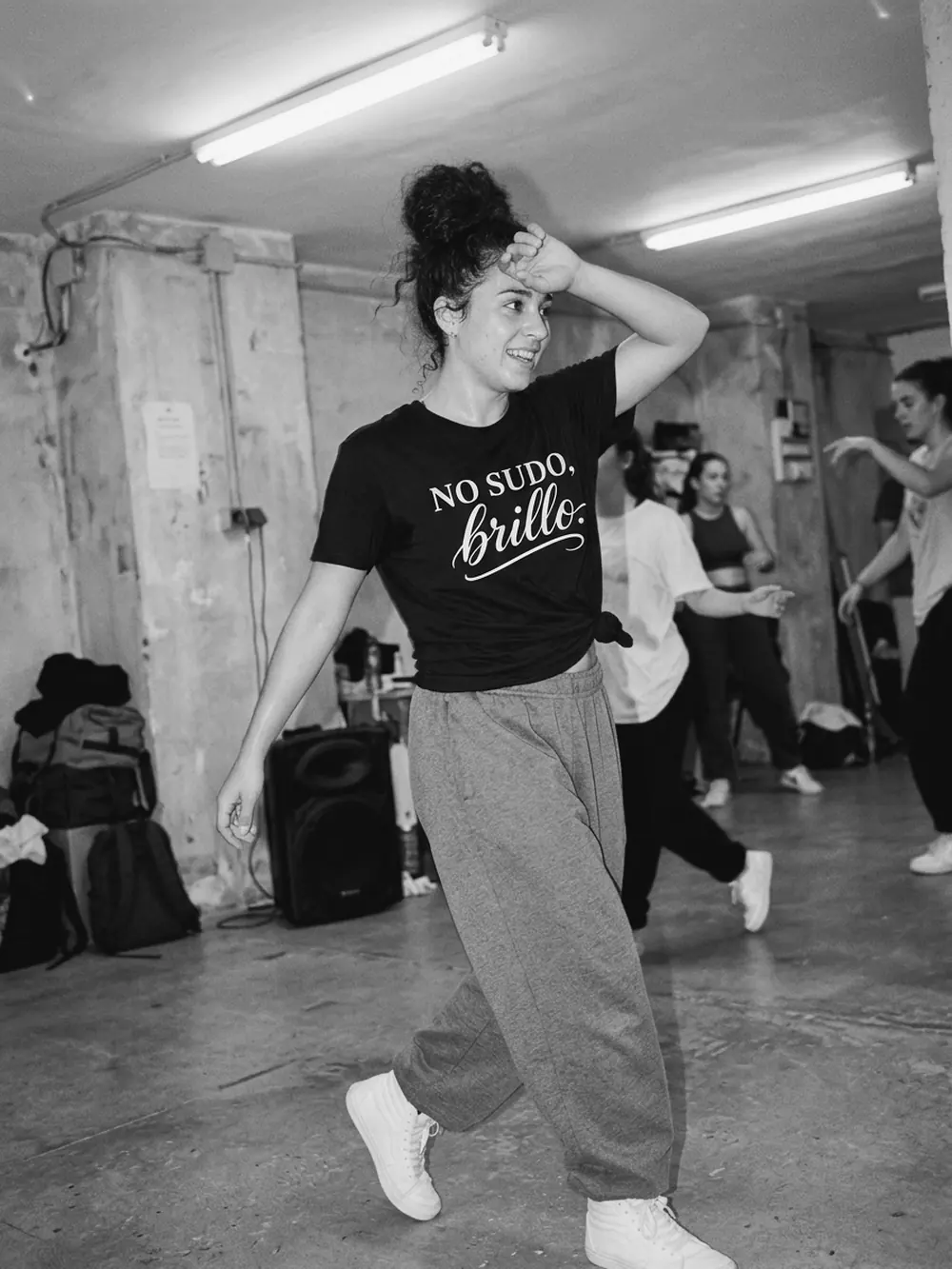 Chica bailando en un local de ensayo con la camiseta negra No sudo, brillo anudada, en blanco y negro