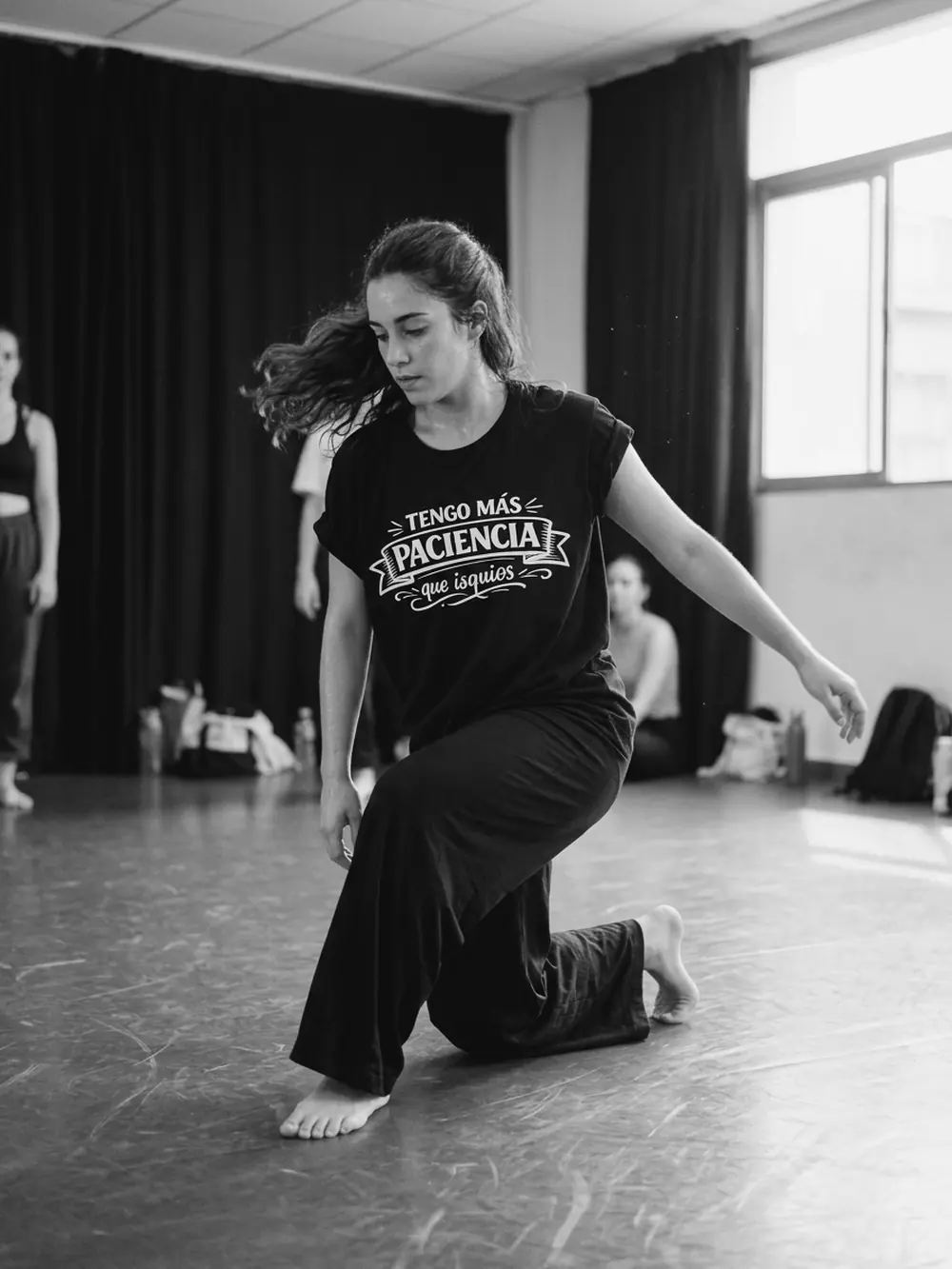 Bailarina de contemporáneo con una rodilla en el suelo, con la camiseta negra Tengo más paciencia que isquios
