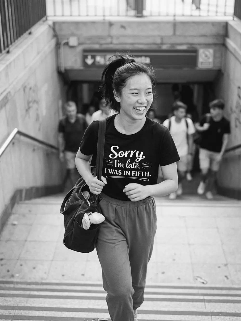 Chica riendo al salir del metro con la camiseta negra Sorry, I'm late. I was in fifth.
