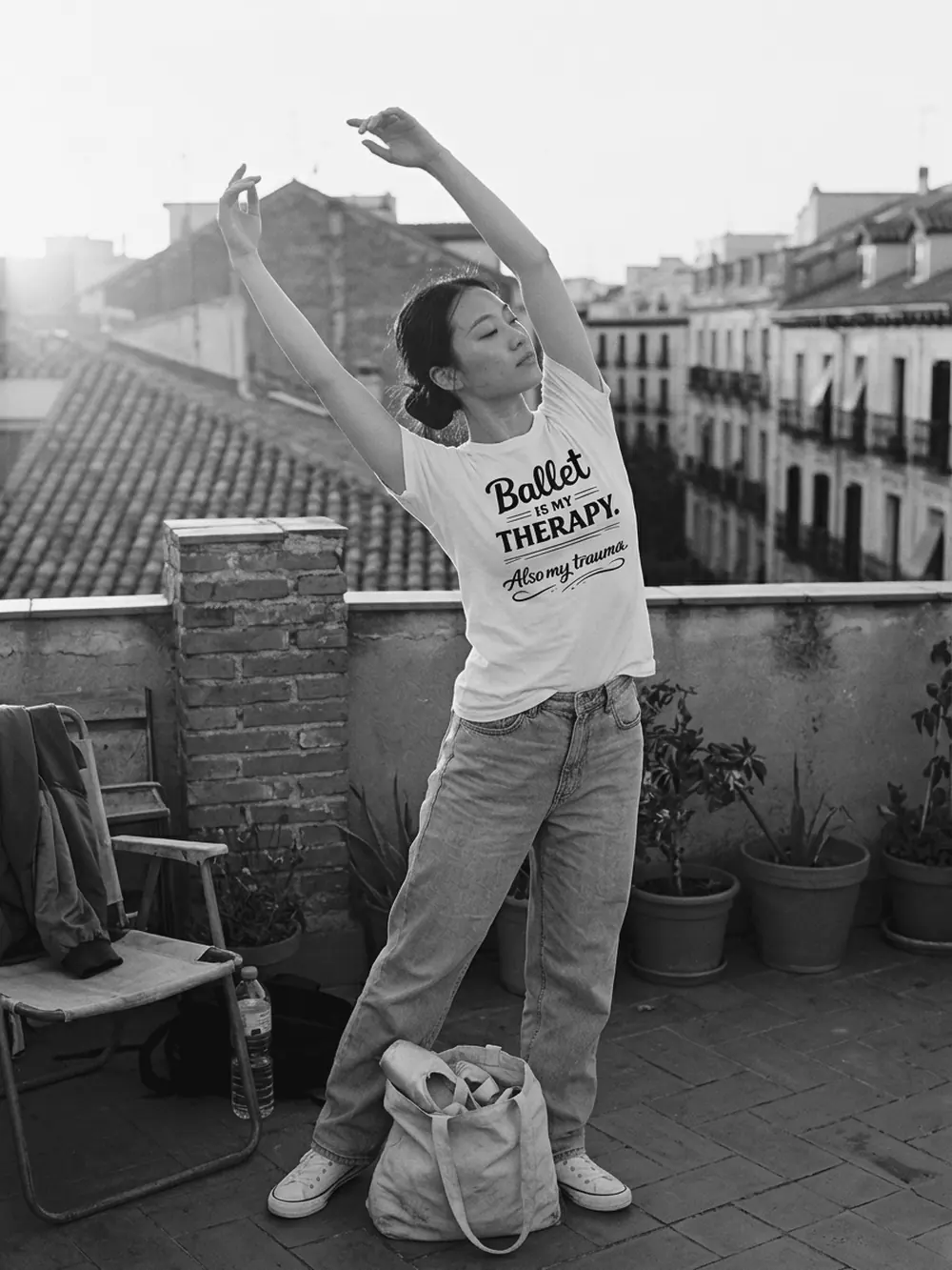 Chica estirando los brazos en una azotea al atardecer, con la camiseta blanca Ballet is my therapy